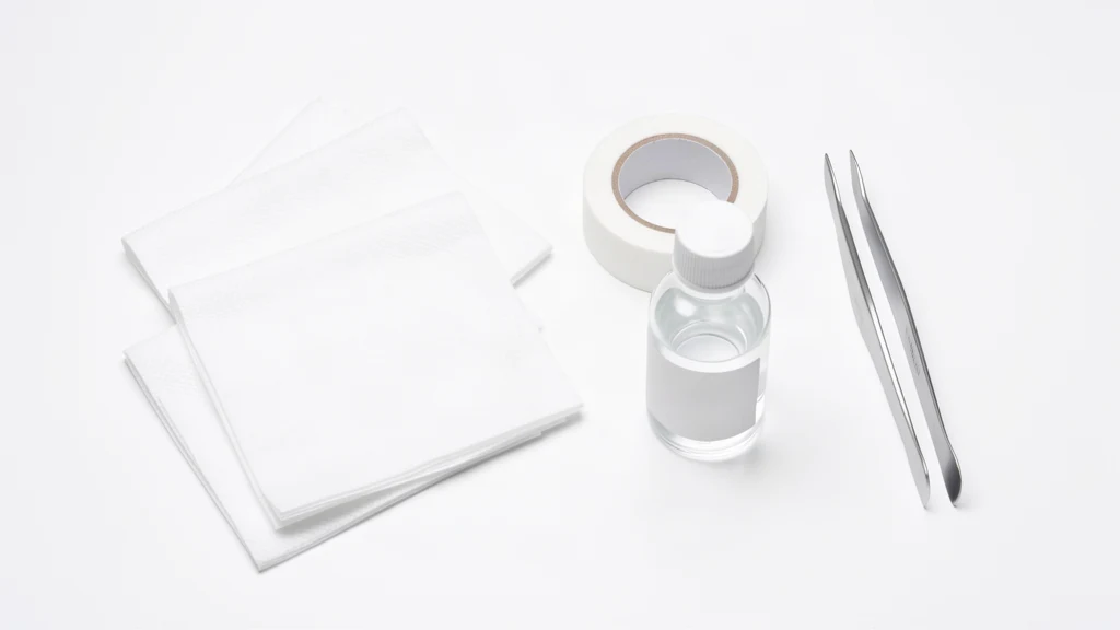 Gauze pads, surgical tape, tweezers and an unlabelled bottle of antiseptic on a white surface